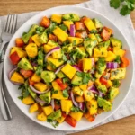 Vibrant Avocado and Mango Salad in a white bowl on a wooden table.